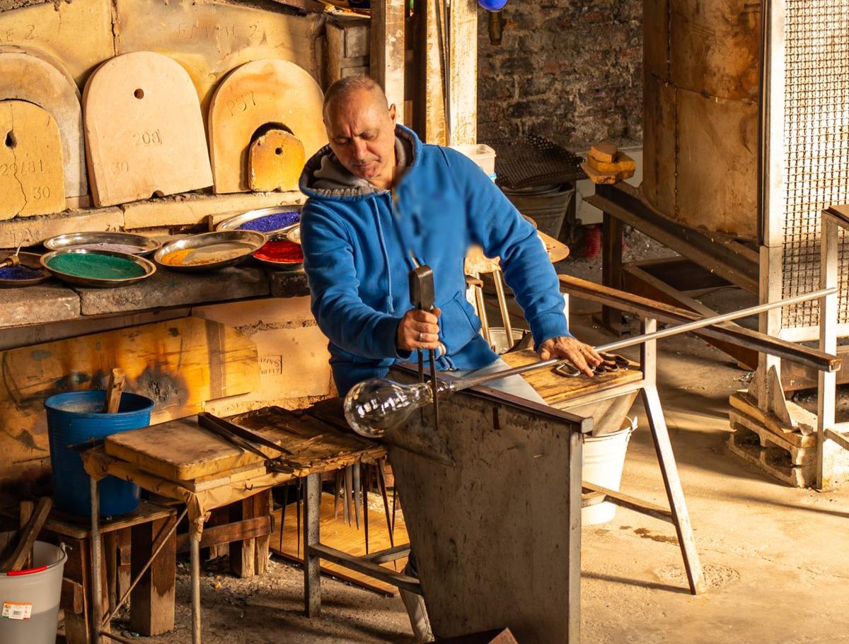 A glassblower shaping glass at his bench in a workshop